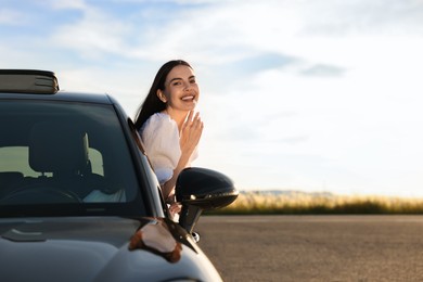 Smiling young woman leaning out of car window outdoors. Enjoying trip