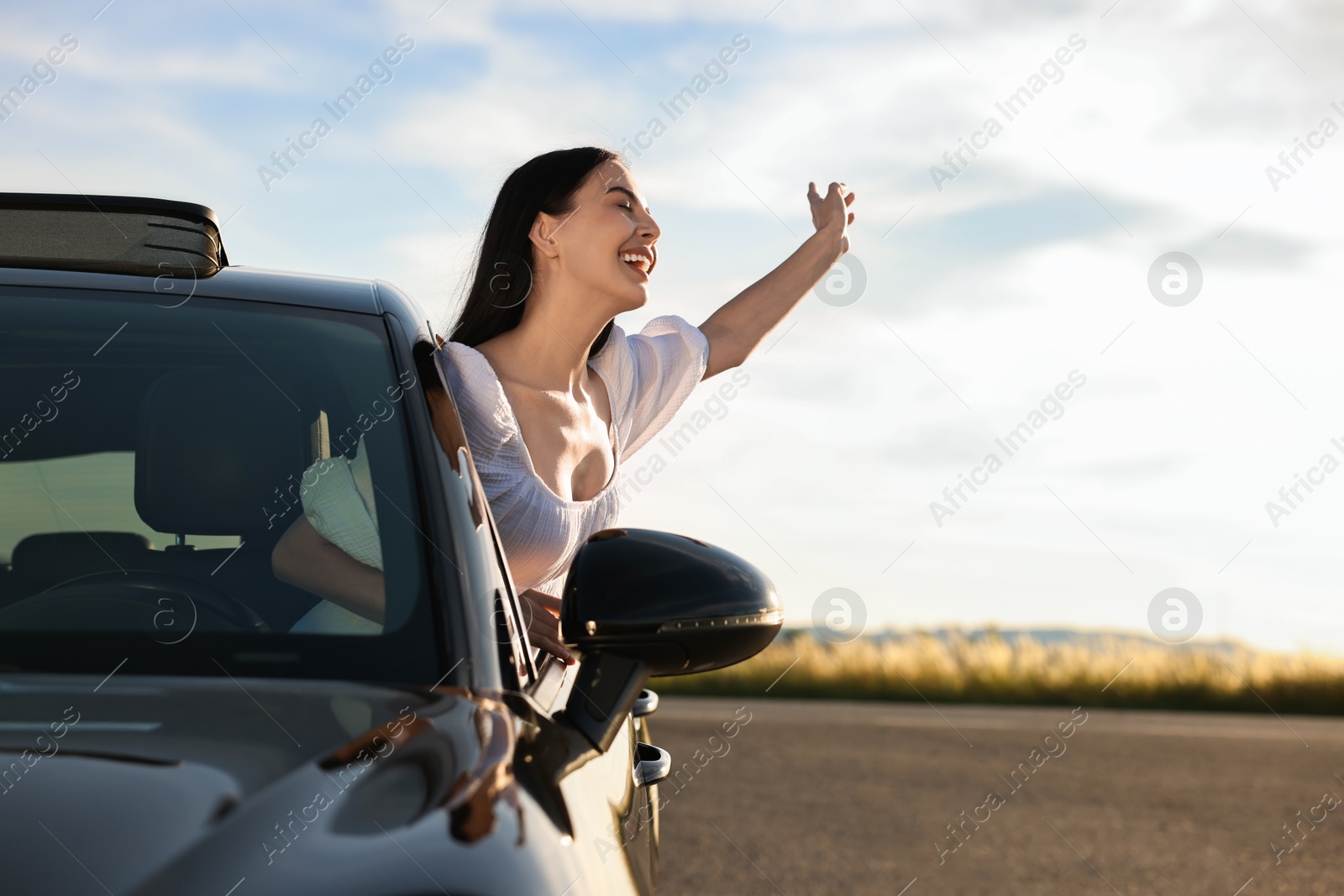 Photo of Smiling young woman leaning out of car window outdoors. Enjoying trip