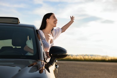 Smiling young woman leaning out of car window outdoors. Enjoying trip