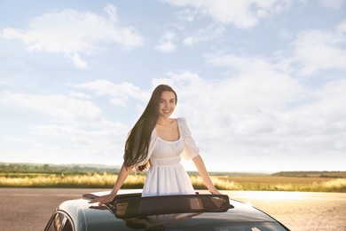 Photo of Enjoying trip. Smiling woman leaning out of car roof outdoors