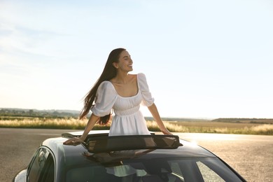 Enjoying trip. Smiling woman leaning out of car roof outdoors