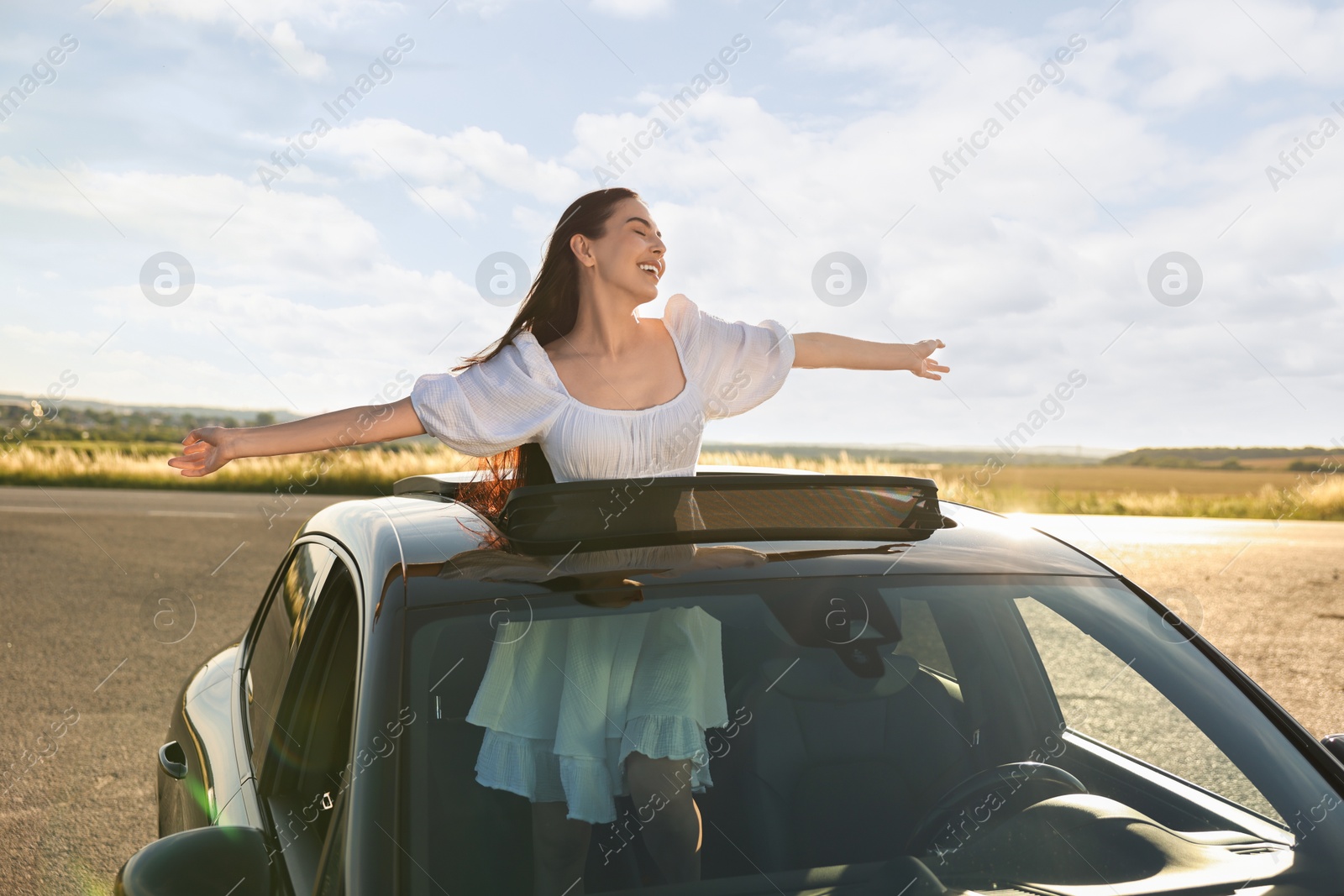 Photo of Enjoying trip. Smiling woman leaning out of car roof outdoors