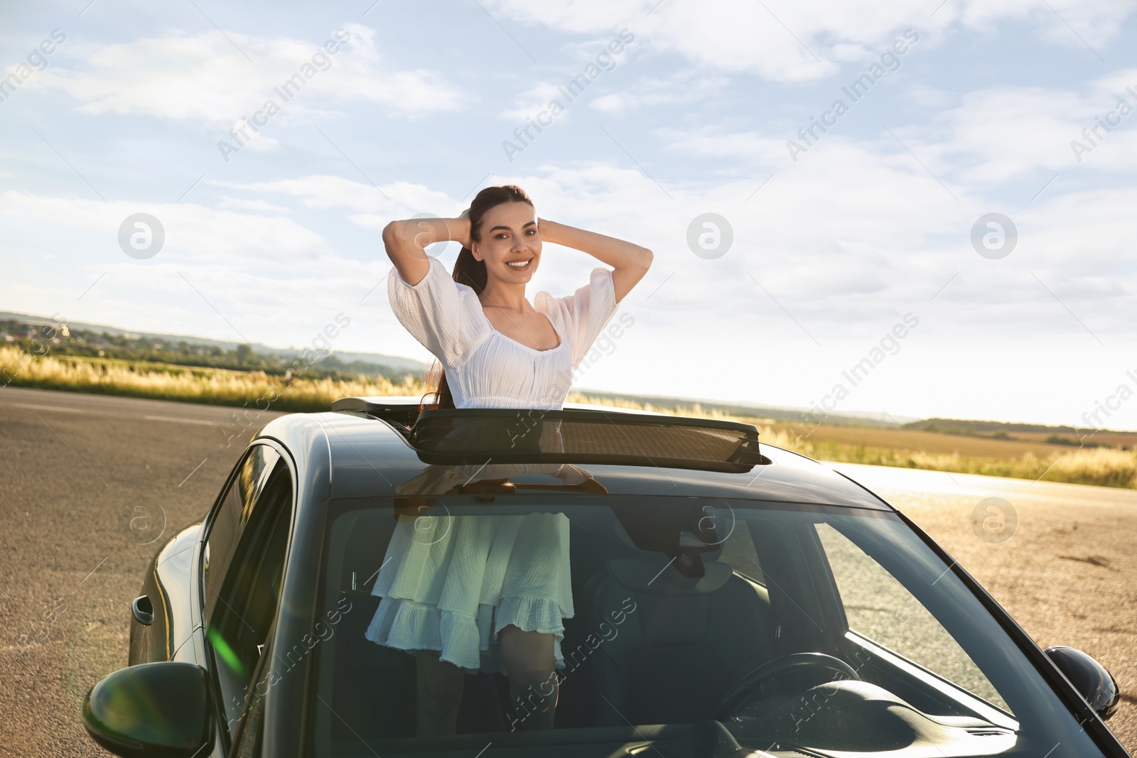 Photo of Enjoying trip. Smiling woman leaning out of car roof outdoors