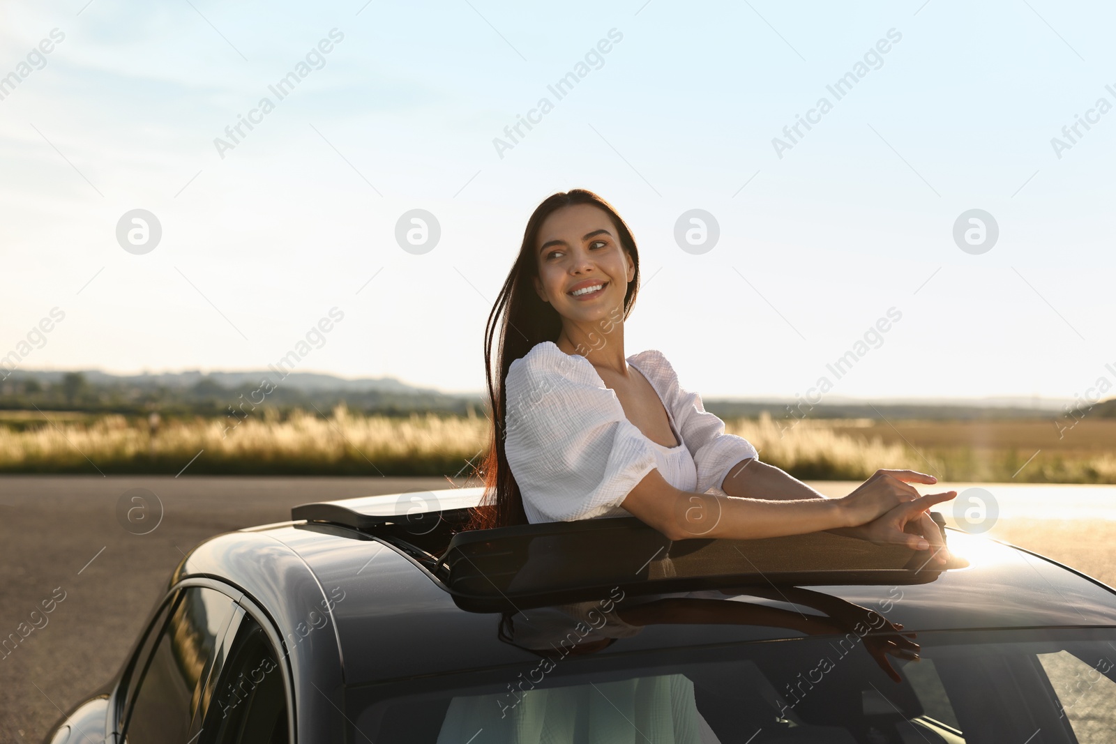 Photo of Enjoying trip. Smiling woman leaning out of car roof outdoors