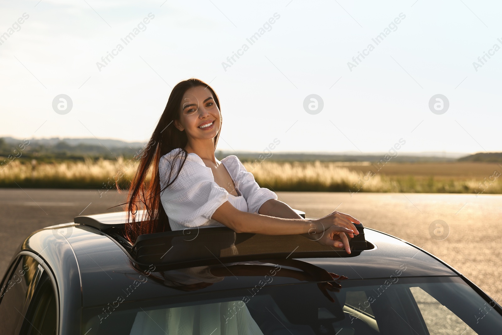 Photo of Enjoying trip. Smiling woman leaning out of car roof outdoors