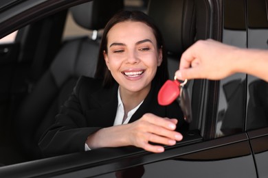 Happy young woman getting key inside her new car