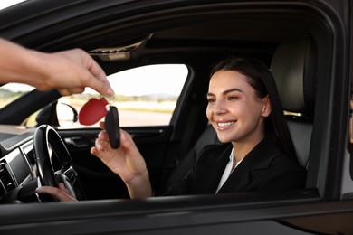 Happy young woman getting key inside her new car