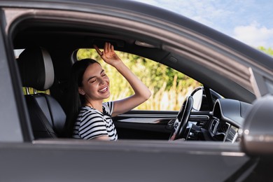 Photo of Smiling young woman having fun while driving car, view from outside