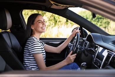 Smiling young woman holding steering wheel while driving car, view from outside