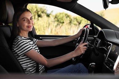 Beautiful young woman holding steering wheel while driving car, view from outside