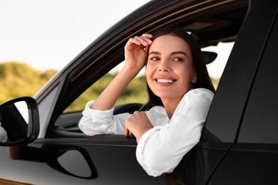 Photo of Smiling young woman leaning out of car window, view from outside. Enjoying trip