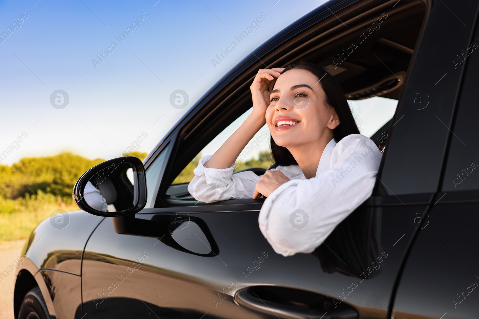 Photo of Smiling young woman leaning out of car window, view from outside. Enjoying trip