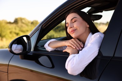 Photo of Beautiful young woman leaning out of car window, view from outside. Enjoying trip