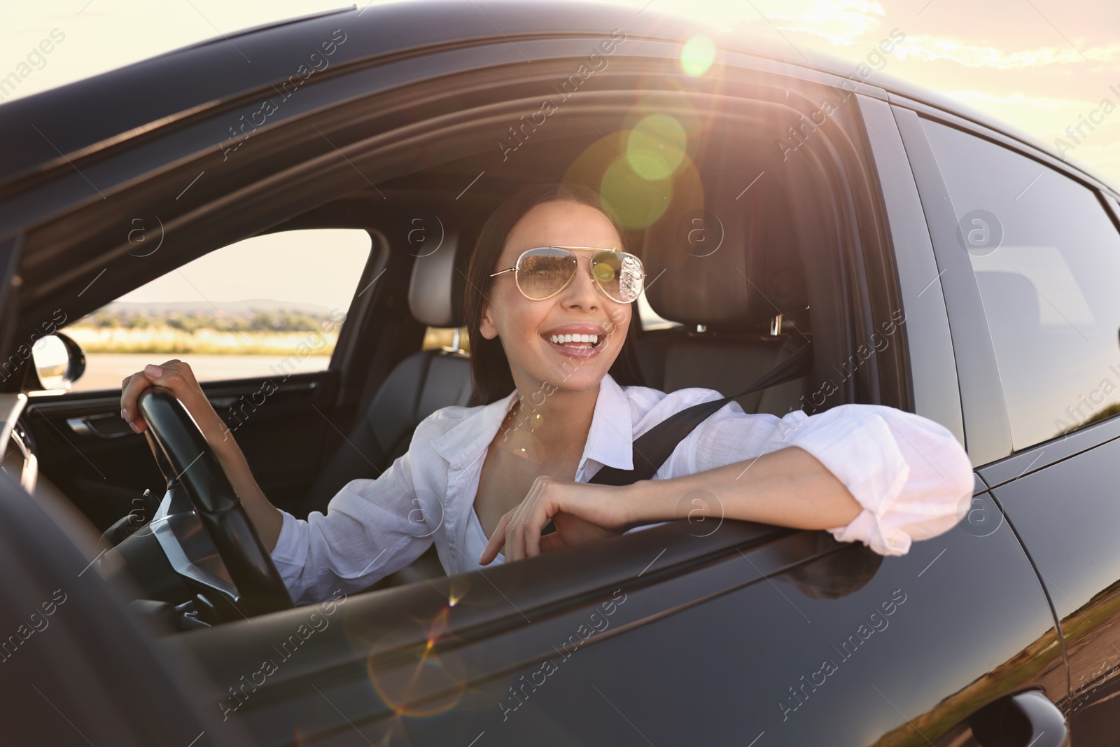 Photo of Smiling young woman in sunglasses with seatbelt driving car, view from outside