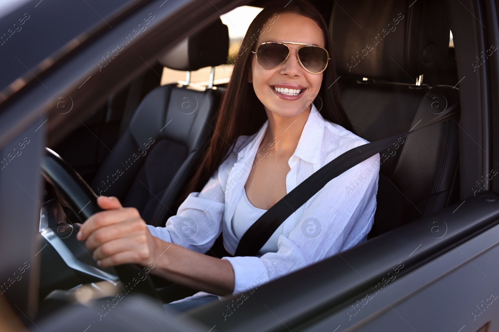 Photo of Smiling young woman in sunglasses with seatbelt driving car, view from outside