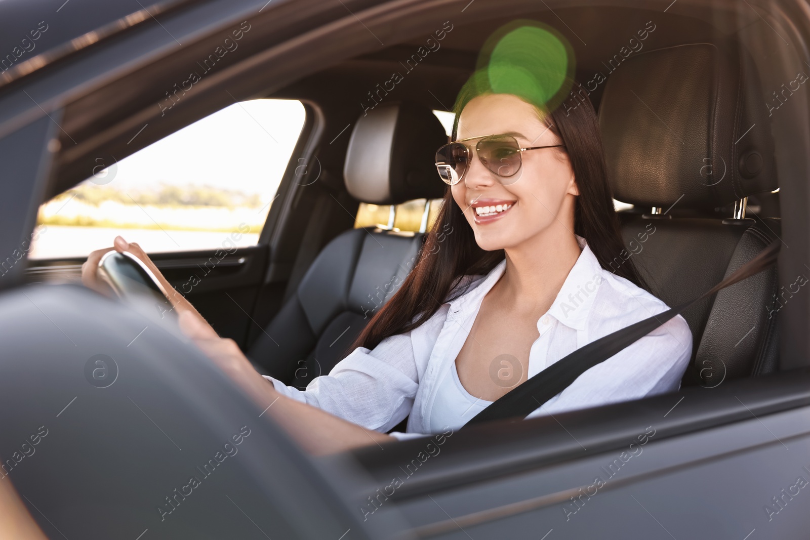 Photo of Smiling young woman in sunglasses with seatbelt driving car, view from outside