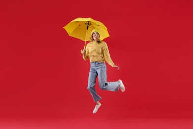 Photo of Woman with yellow umbrella jumping on red background