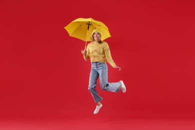 Woman with yellow umbrella jumping on red background