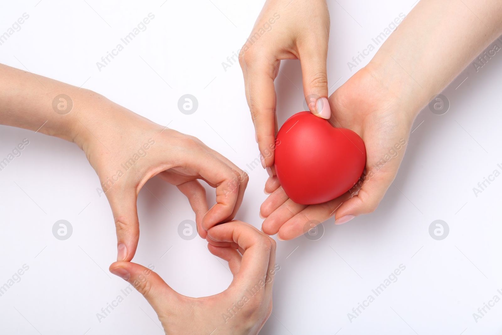 Photo of Women holding red heart figure and showing heart gesture at white table, top view