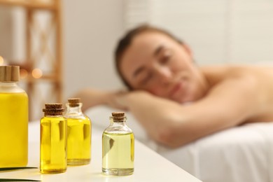 Aromatherapy. Woman relaxing on massage couch in spa salon, focus on bottles of essential oils