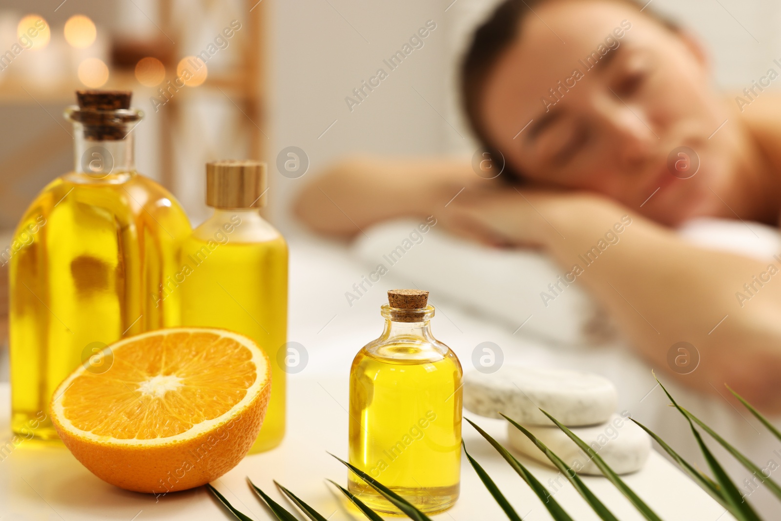 Photo of Aromatherapy. Woman relaxing on massage couch in spa salon, focus on bottles of essential oils, orange and stones