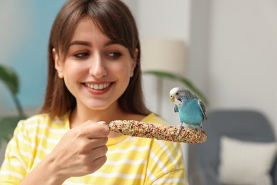 Photo of Woman feeding bright parrot indoors. Exotic pet