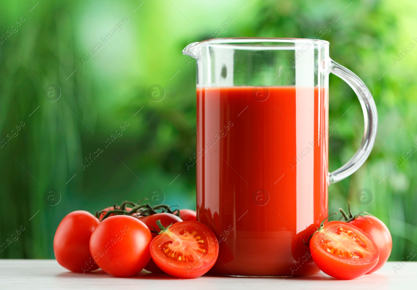 Photo of Tasty tomato juice in glass jug and fresh vegetables on white table outdoors