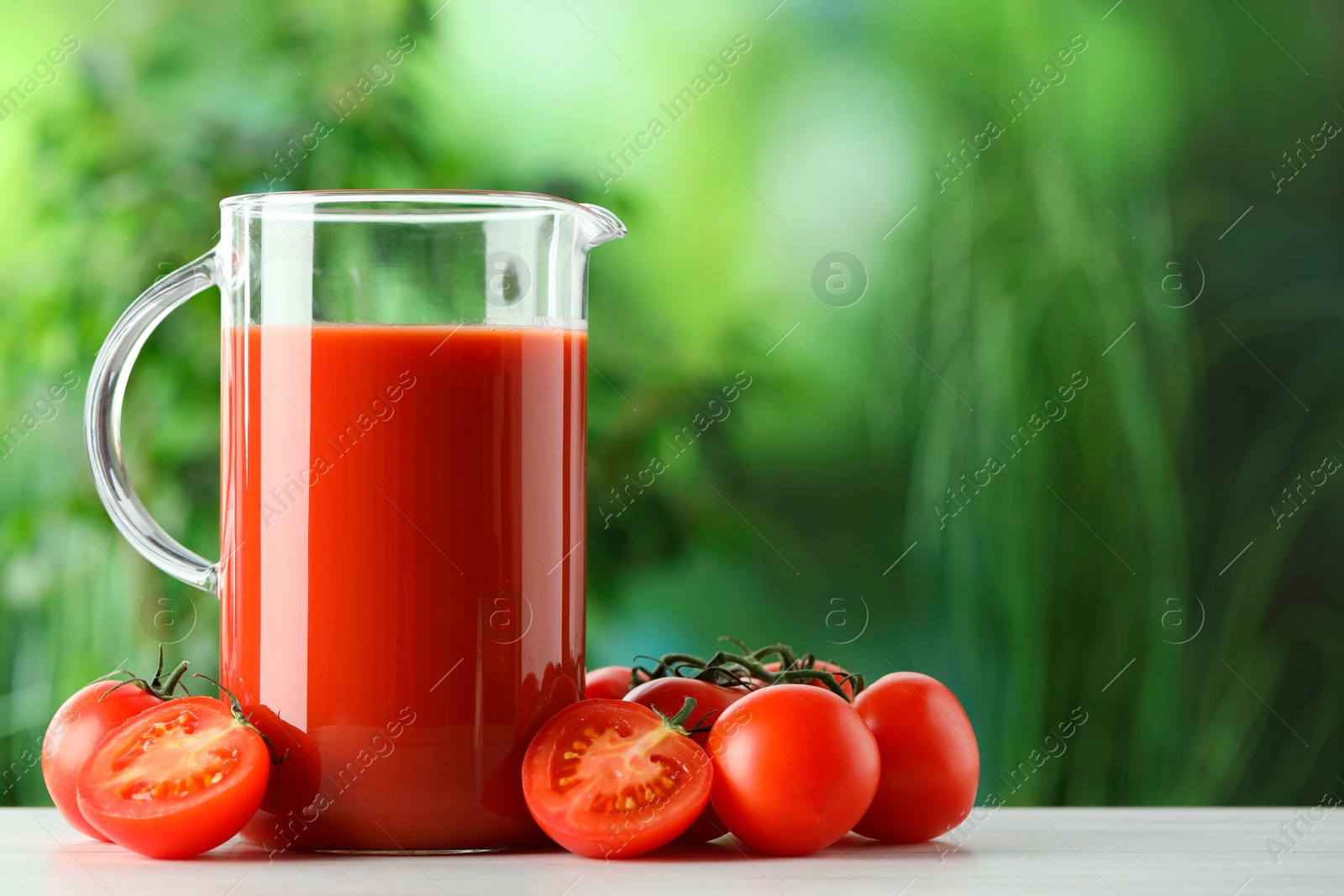 Photo of Tasty tomato juice in glass jug and fresh vegetables on white table outdoors. Space for text