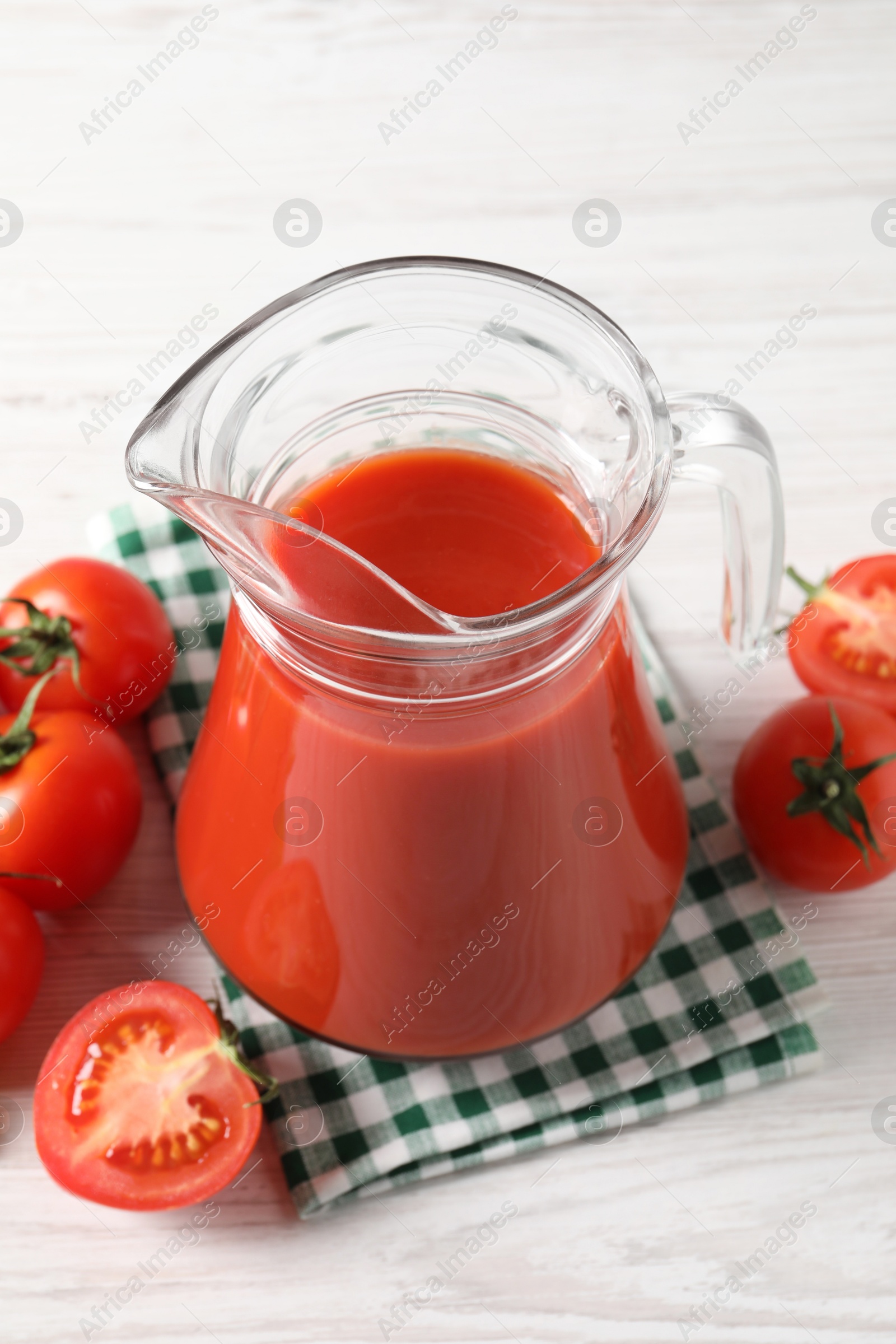 Photo of Tasty tomato juice in glass jug and fresh vegetables on white wooden table