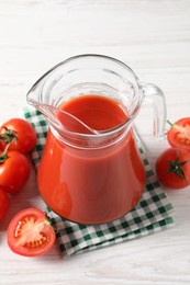 Photo of Tasty tomato juice in glass jug and fresh vegetables on white wooden table