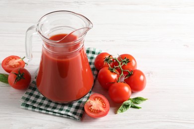 Photo of Tasty tomato juice in glass jug and fresh vegetables on white wooden table. Space for text