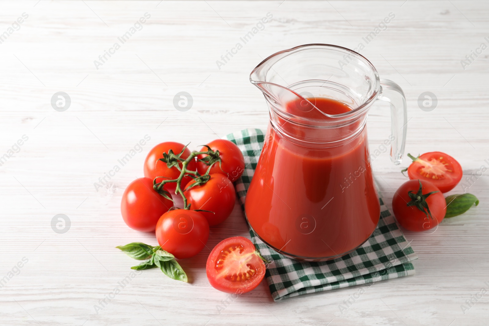 Photo of Tasty tomato juice in glass jug and fresh vegetables on white wooden table