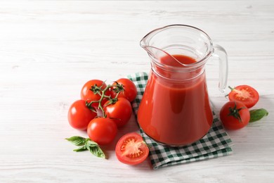 Photo of Tasty tomato juice in glass jug and fresh vegetables on white wooden table