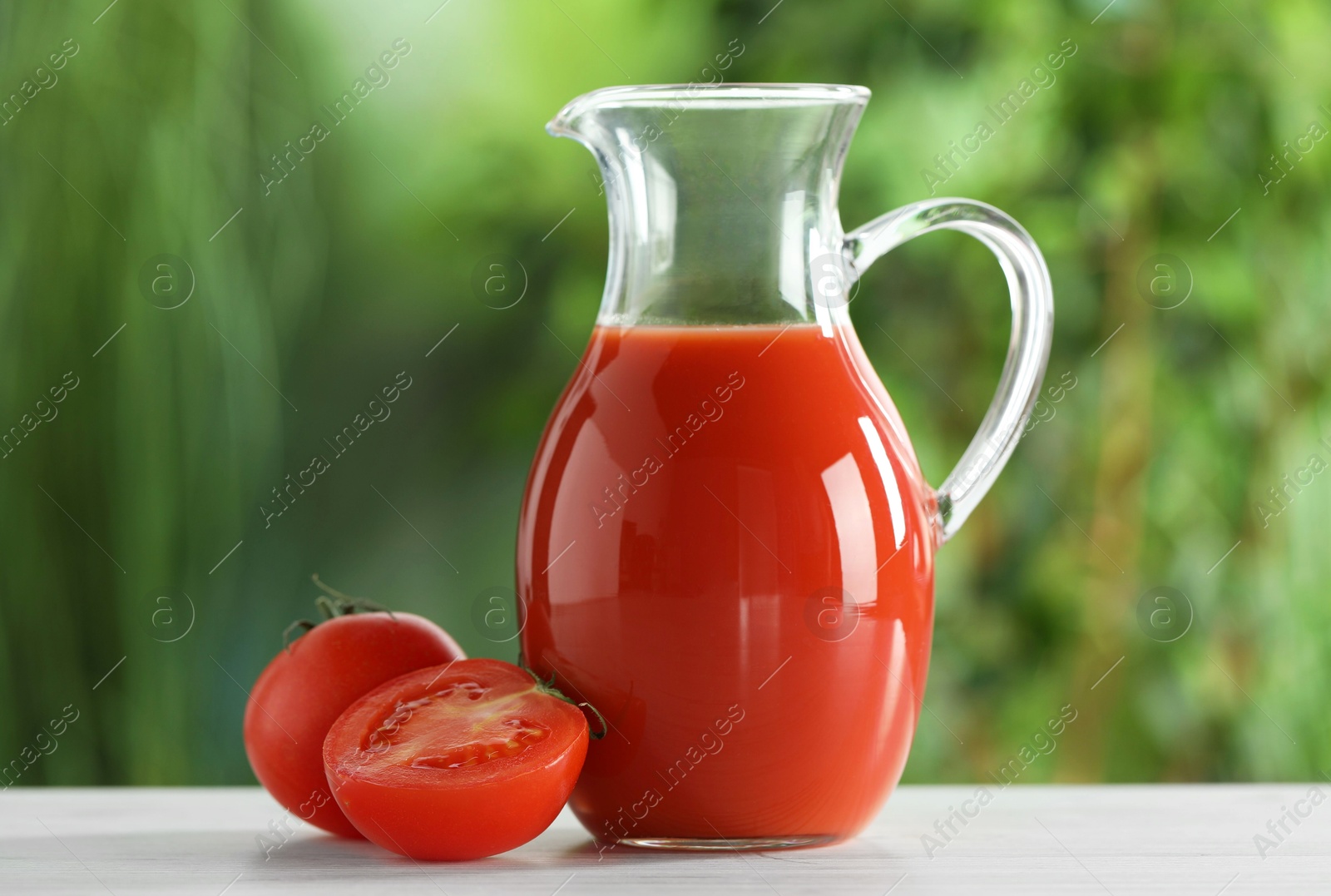 Photo of Tasty tomato juice in glass jug and fresh vegetables on white table outdoors