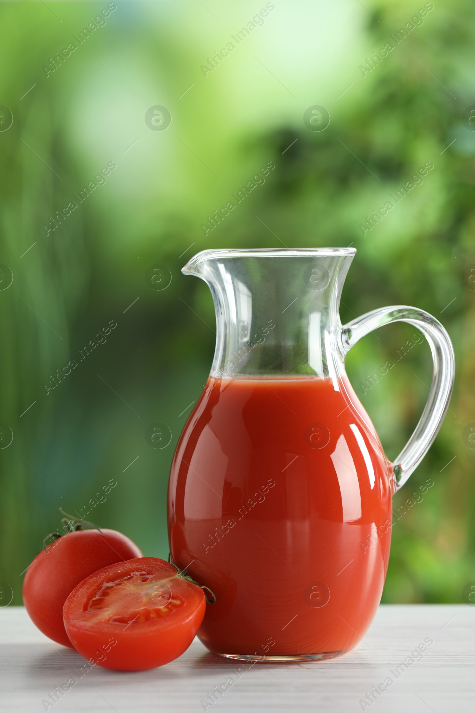 Photo of Tasty tomato juice in glass jug and fresh vegetables on white table outdoors