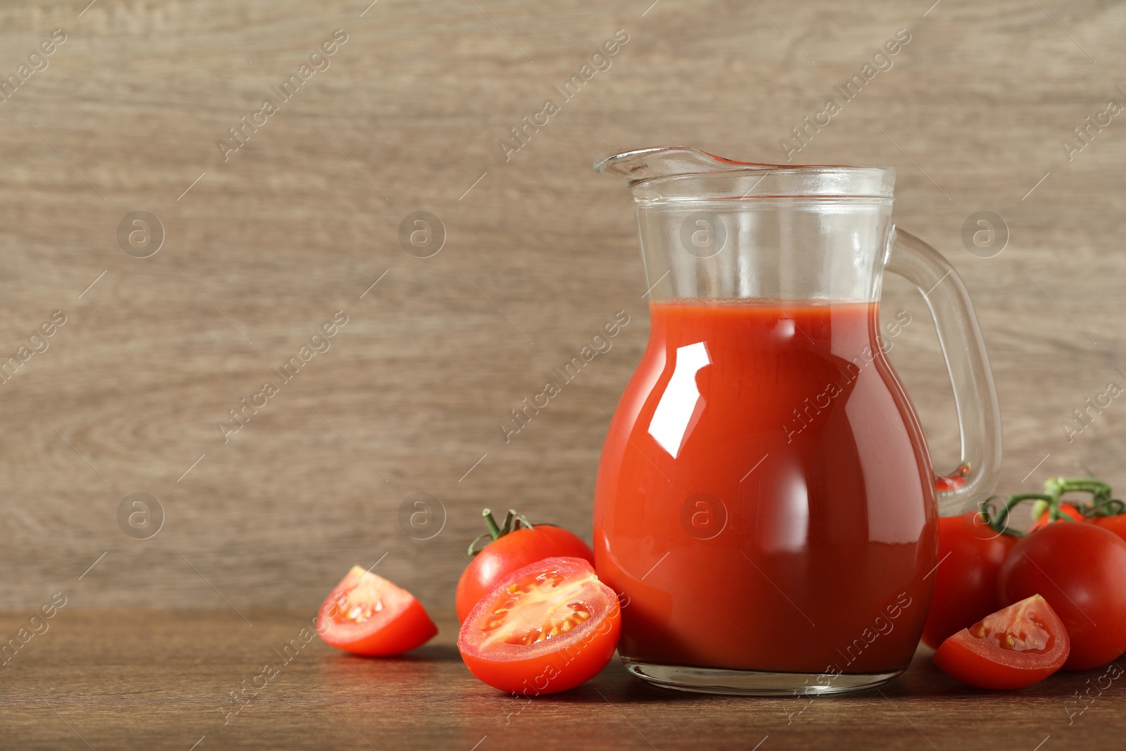 Photo of Tasty tomato juice in jug and vegetables on wooden table. Space for text