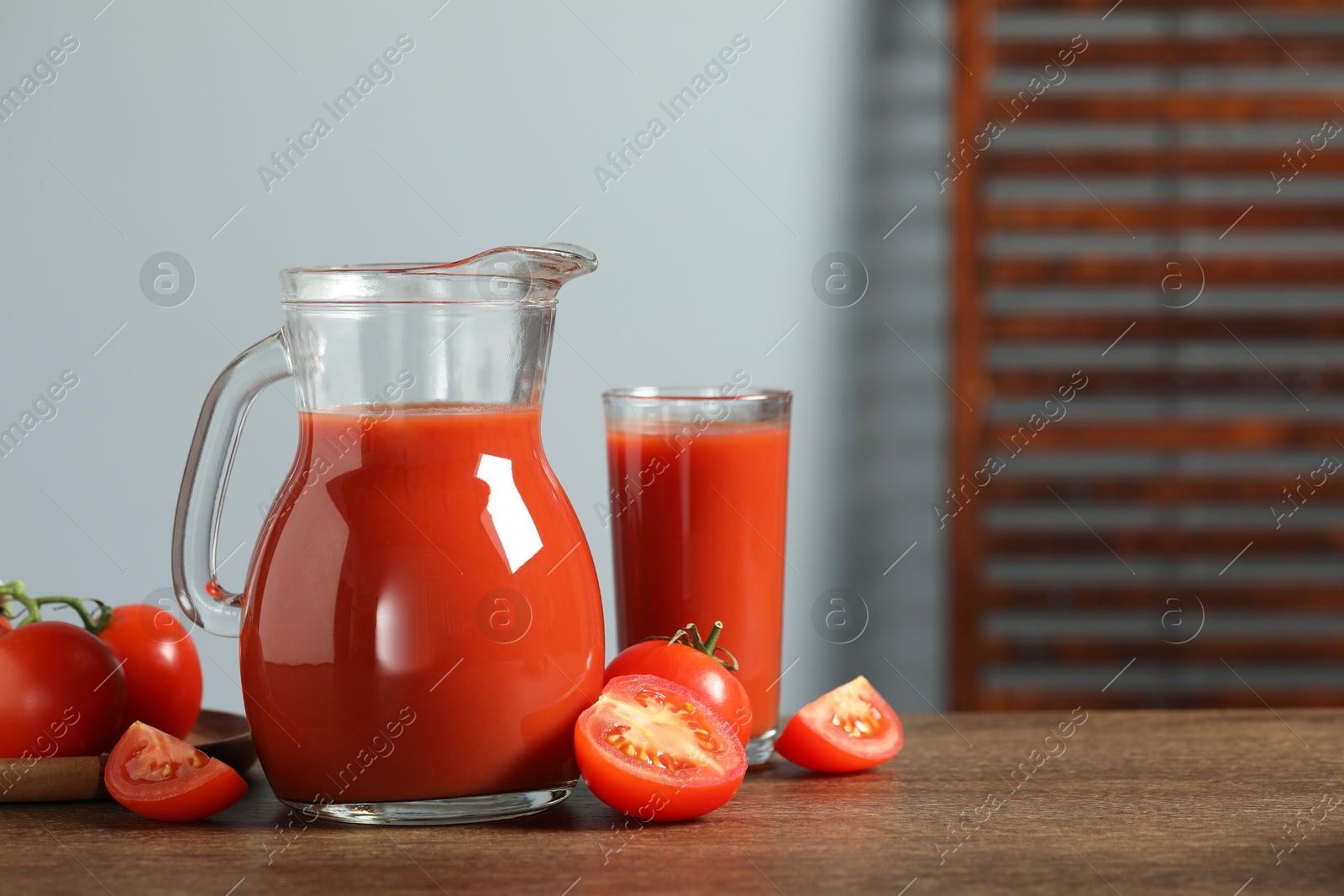 Photo of Tasty tomato juice in jug, glass and vegetables on wooden table. Space for text