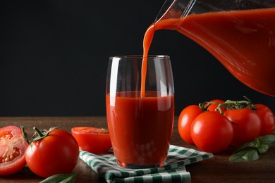 Photo of Pouring tasty tomato juice from jug into glass at wooden table with vegetables