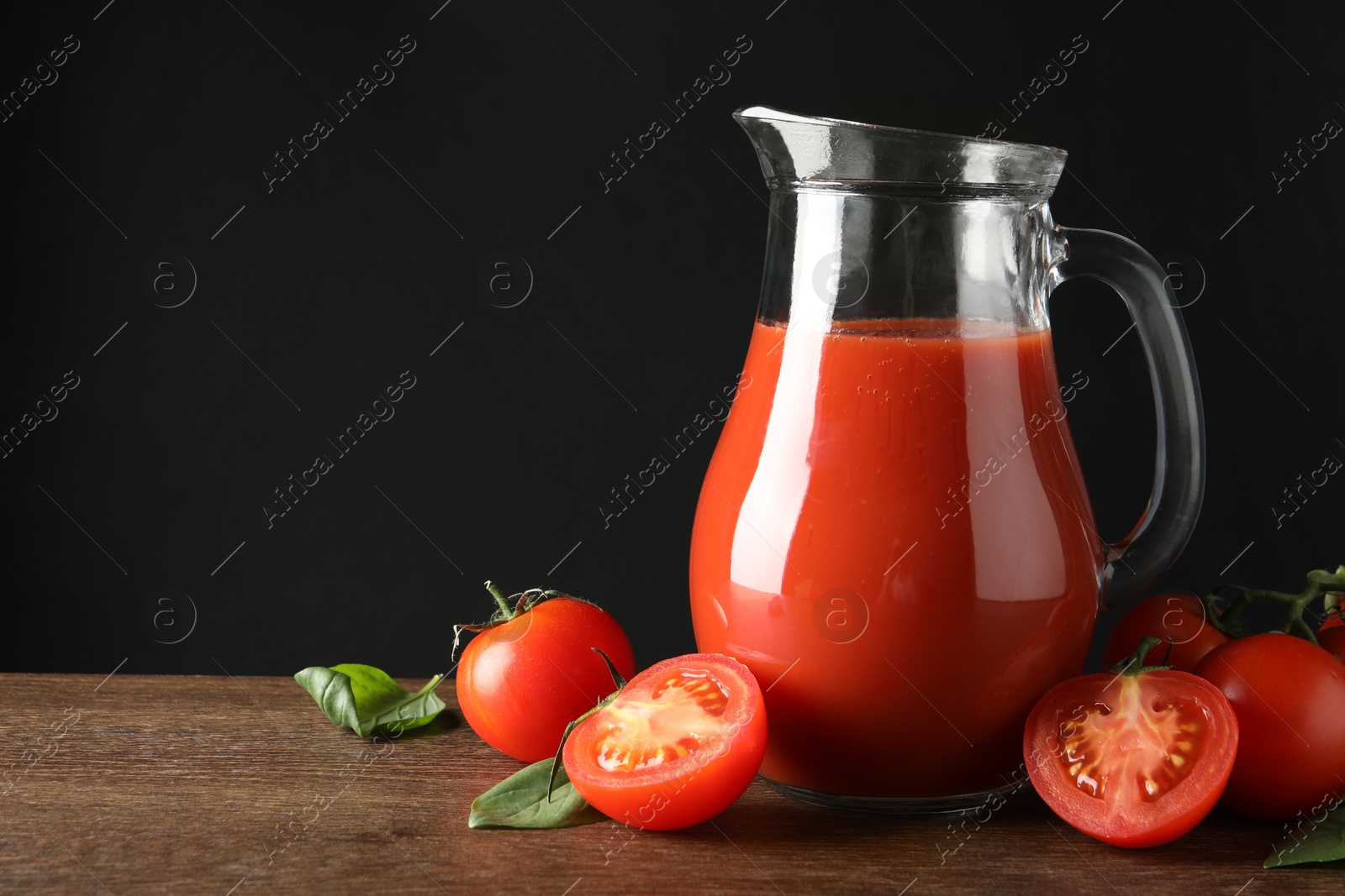 Photo of Tasty tomato juice in jug and vegetables on wooden table against black background. Space for text