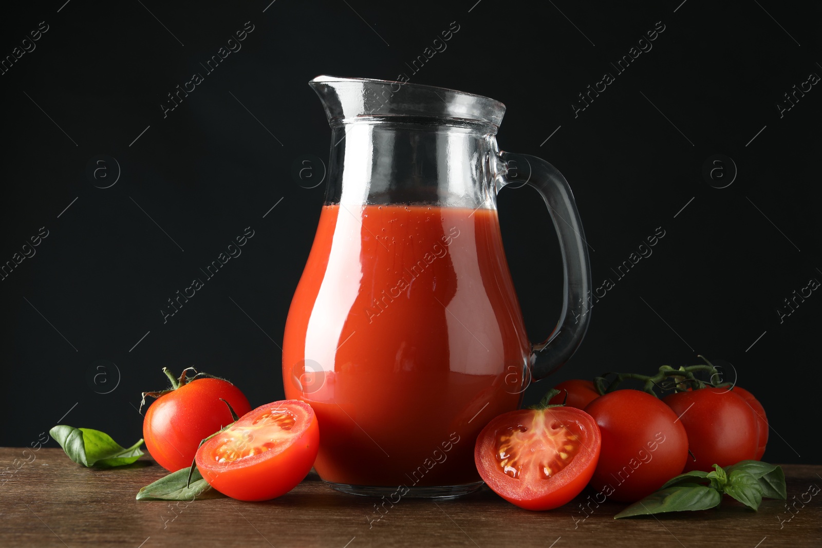 Photo of Tasty tomato juice in jug and vegetables on wooden table against black background