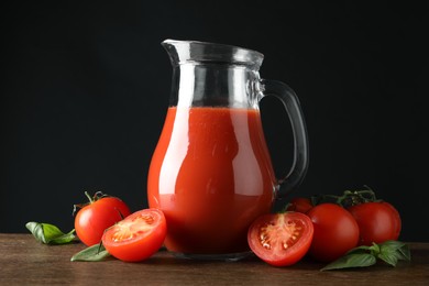 Photo of Tasty tomato juice in jug and vegetables on wooden table against black background