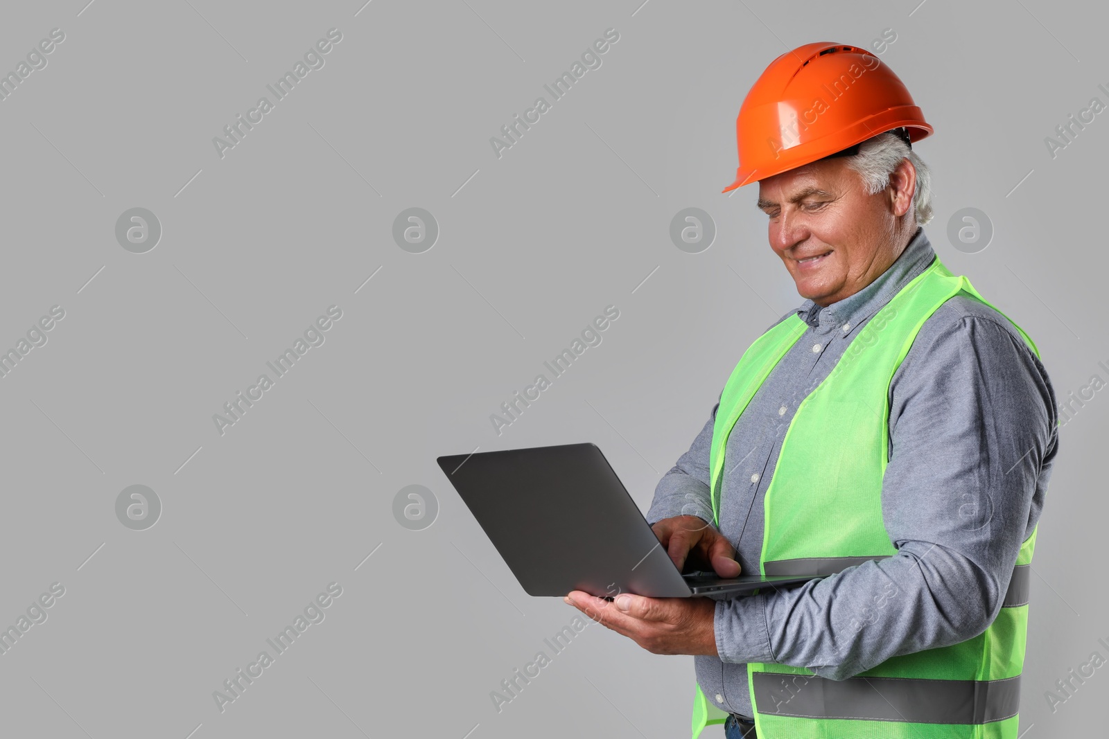 Photo of Engineer in hard hat with laptop on grey background, space for text