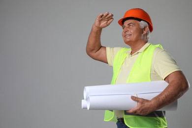 Engineer in hard hat with drafts on grey background, space for text