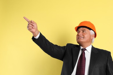 Engineer in hard hat pointing at something on yellow background