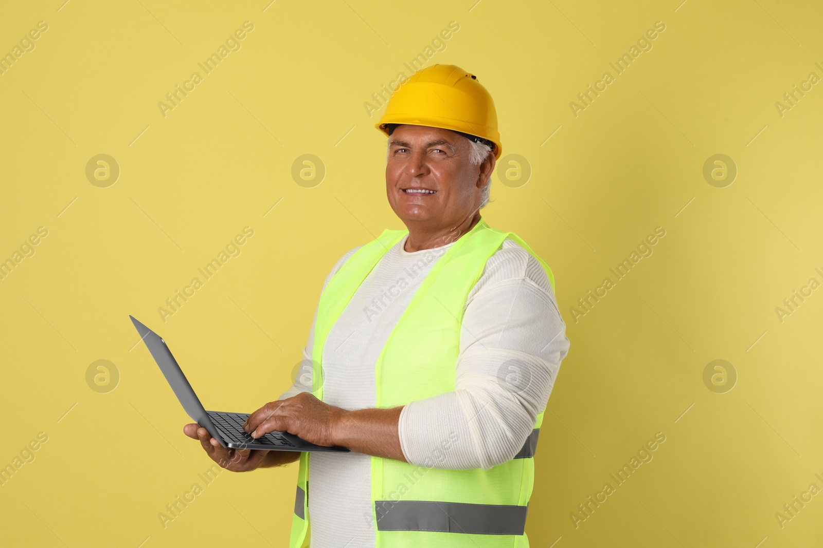 Photo of Engineer in hard hat with laptop on yellow background