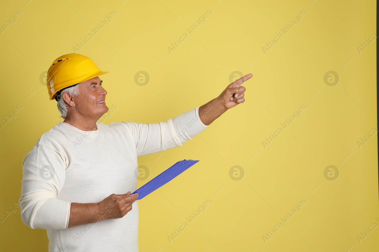 Photo of Engineer in hard hat with clipboard on yellow background, space for text