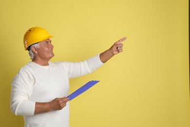 Photo of Engineer in hard hat with clipboard on yellow background, space for text