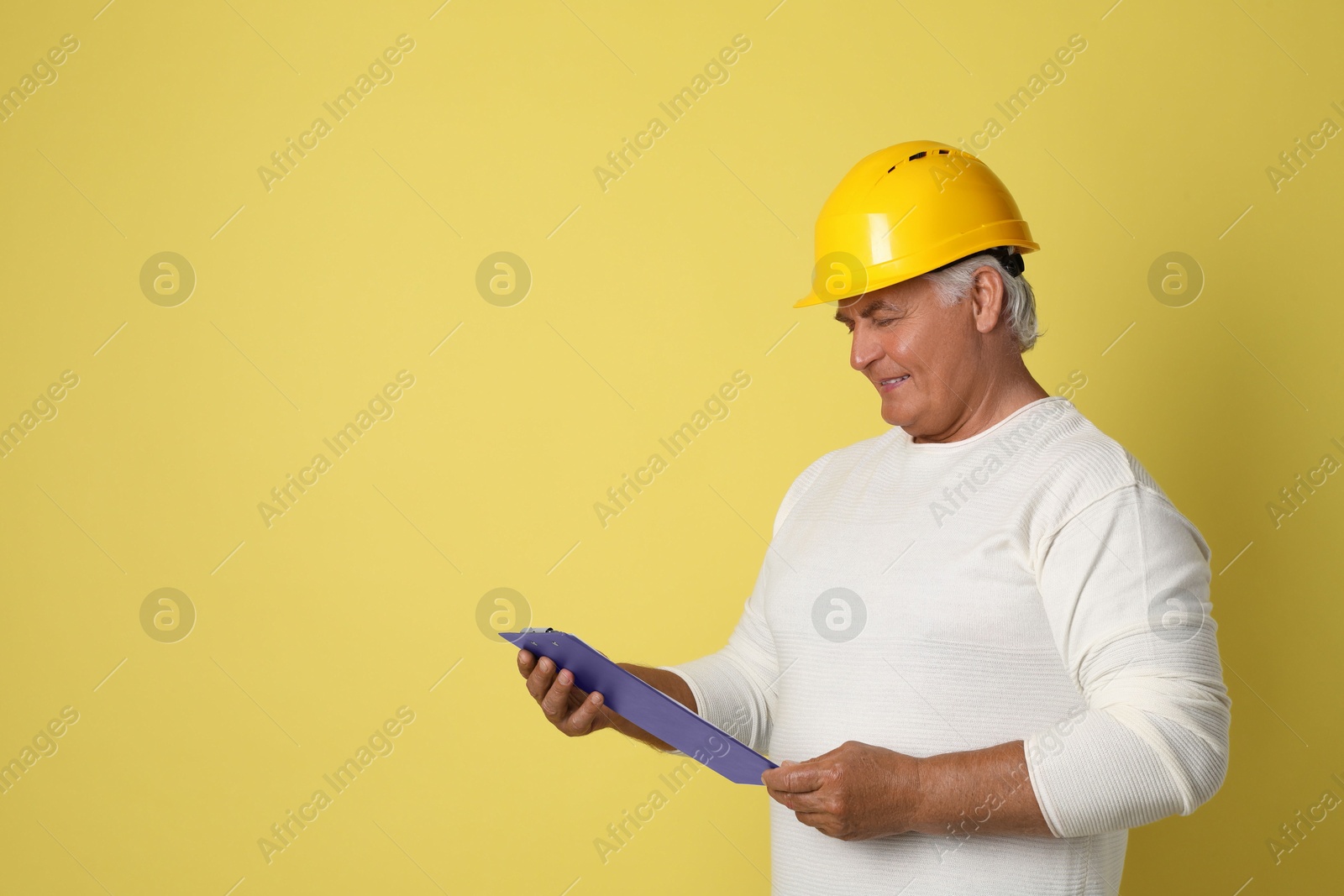 Photo of Engineer in hard hat with clipboard on yellow background, space for text