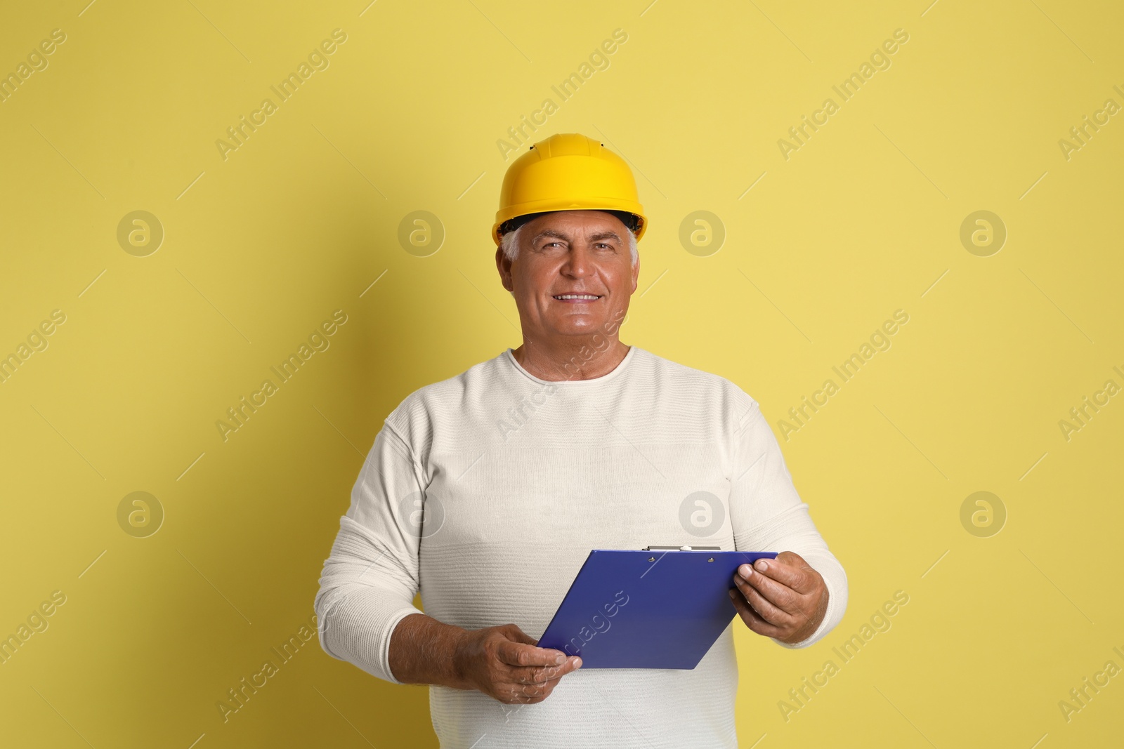 Photo of Engineer in hard hat with clipboard on yellow background