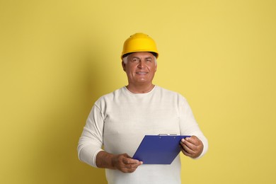 Engineer in hard hat with clipboard on yellow background